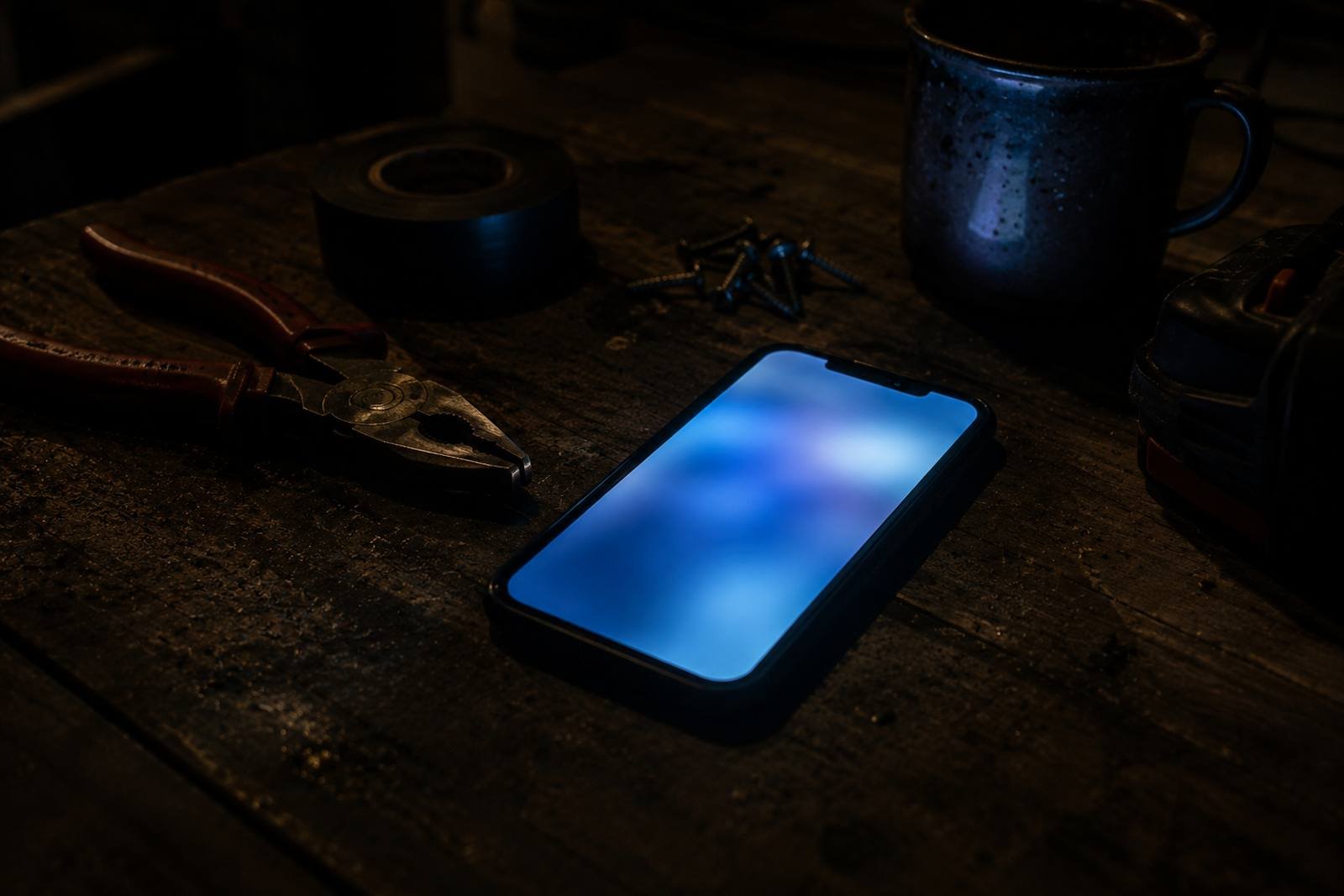 A phone face up on a timber workbench in a dark shed, its screen the only light in the frame