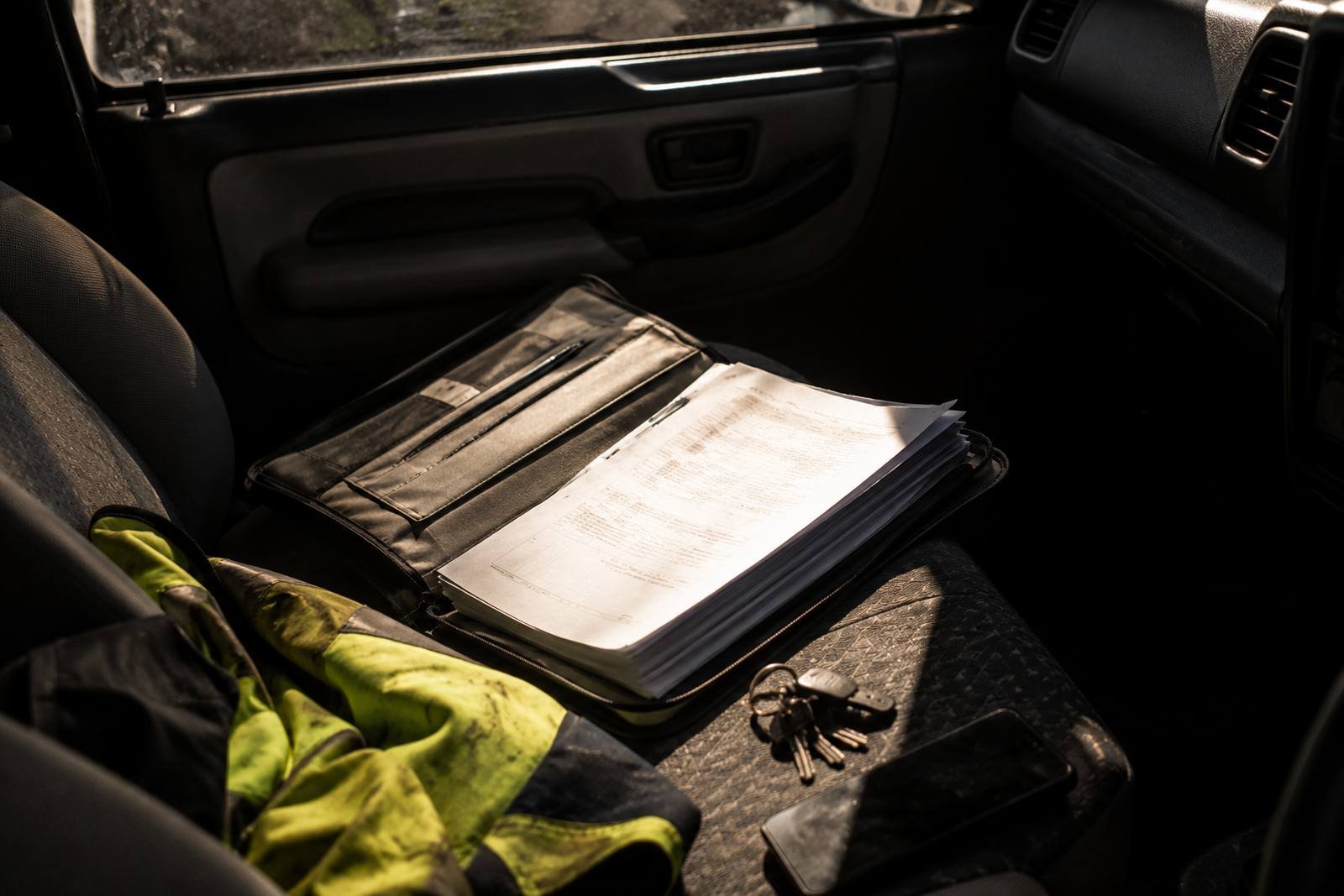 An open document wallet of stapled paperwork on the passenger seat of a work ute, catching hard sun