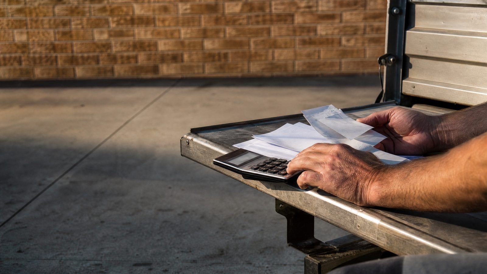 Hands working a calculator beside a pile of receipts on a ute tailgate