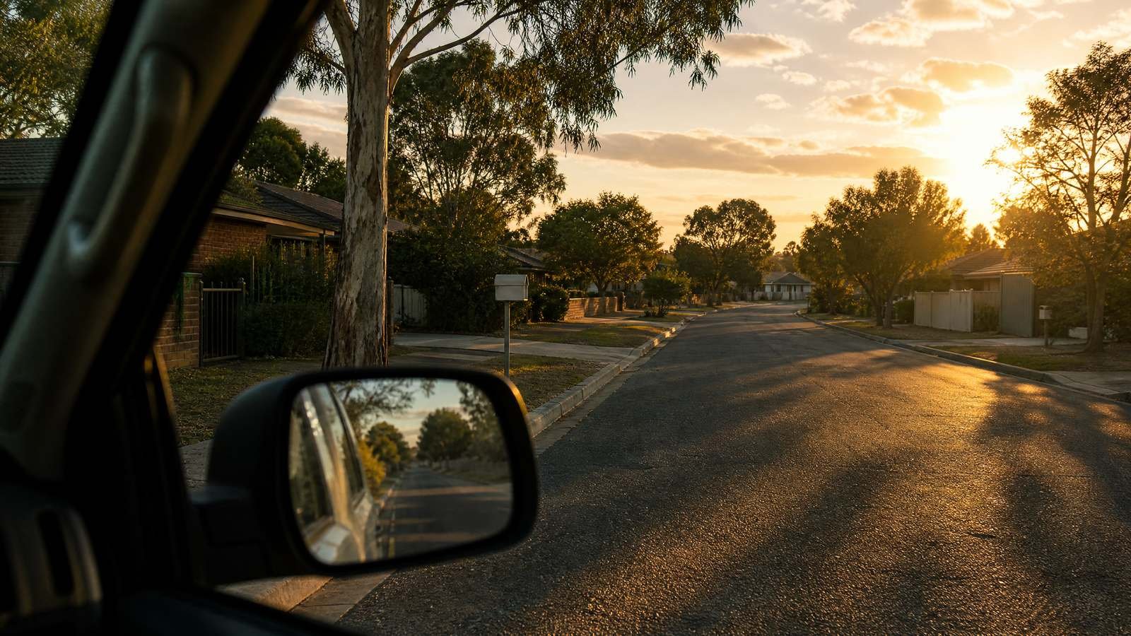 Looking down a quiet Australian suburban street from the driver's window of a parked work ute at sunset