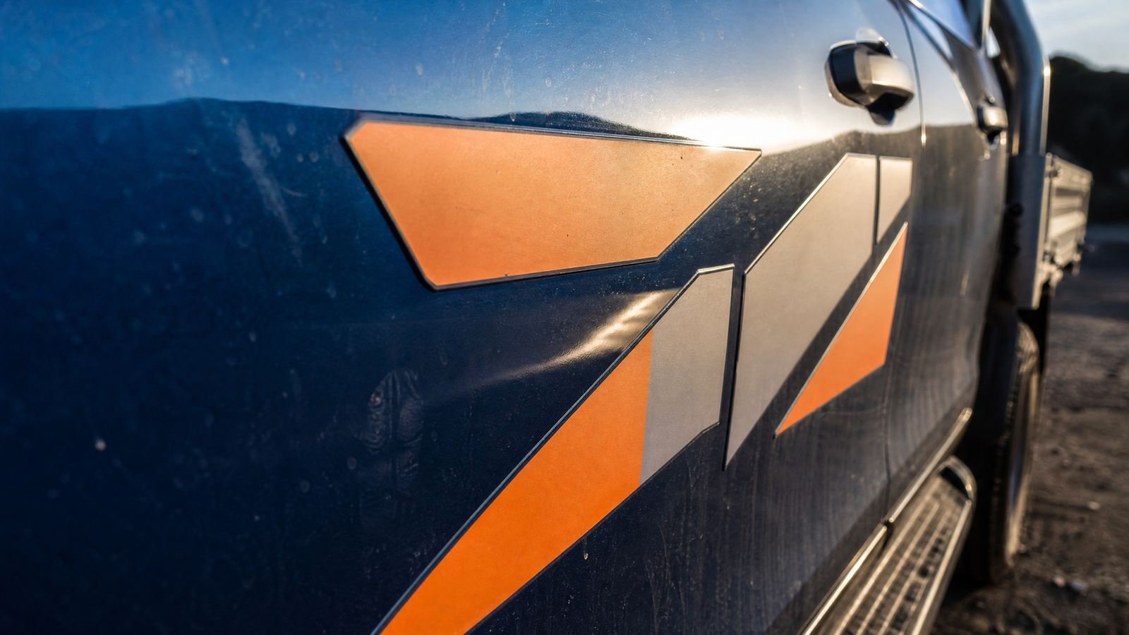 Close on the door of a work ute with fresh cut-vinyl signwriting, low sun raking across the edge of the vinyl